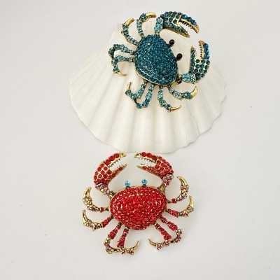 Brincos ou pins caranguejo decorados com pedras azuis e vermelhas em fundo branco