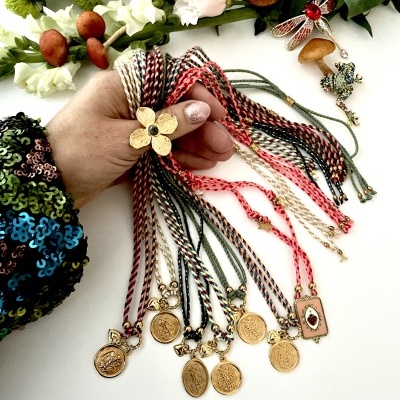 Pulseiras coloridas com pendentes de moedas seguradas por mão feminina com flores ao fundo