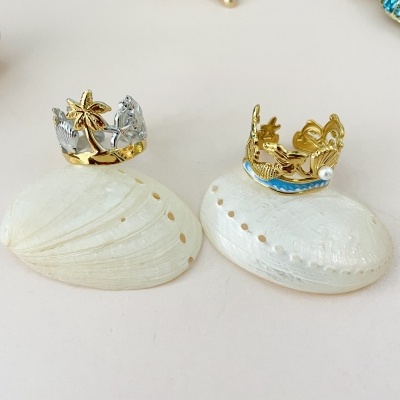 Anéis com tema marinho sobre conchas brancas e fundo neutro.