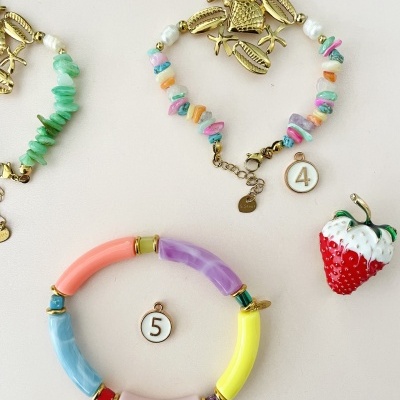 Duas pulseiras coloridas e um broche de morango sobre fundo branco.