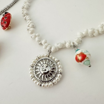 Colar com pendentes de joaninha, sol prateado e contas brancas com floral vermelho