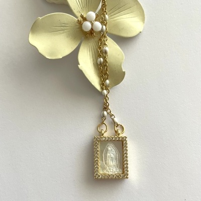 Colar dourado com pendente retangular com imagem religiosa e flor amarela ao fundo