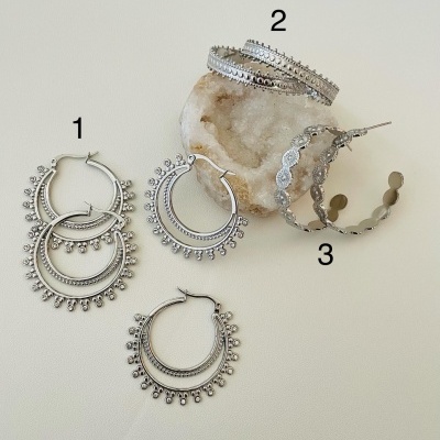 Três pares de brincos de argola prateados com padrões decorativos e uma pedra bege, sobre fundo claro