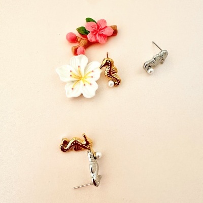 Brincos de cavalo-marinho dourado e carro prateado com pérola, sobre fundo bege com flores decorativas