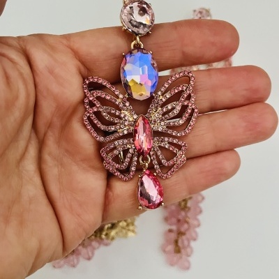 Brinco pendente com pedras coloridas e strass rosa em forma de borboleta na mão