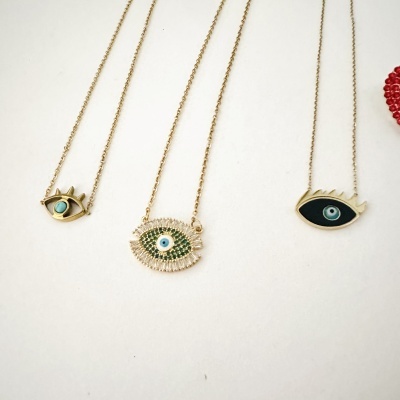 Três colares dourados com pendentes em forma de olho em fundo branco.