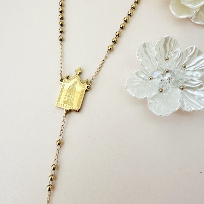 Colar dourado com pendente religioso e flores brancas ao lado