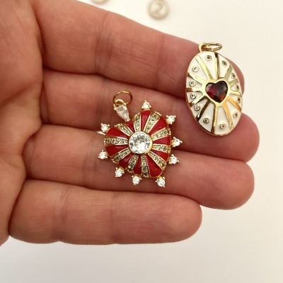 Dois pendentes dourados com pedras, um vermelho circular e outro oval com coração vermelho