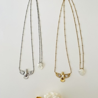 Dois colares com pendentes de anjo e coração sobre fundo branco, com flor decorativa