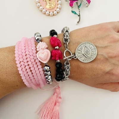 Pulseiras coloridas em braço e dois broches ao fundo sobre superfície branca