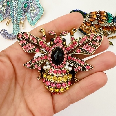Broche abelha com cristais rosa, amarelos, pérolas e pedra negra segurado em mão.