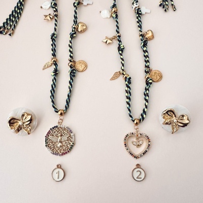 Dois colares com pendentes dourados e brincos laço sobre fundo branco