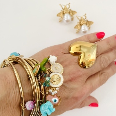 Mão com pulseiras douradas, anel coração dourado, brincos abelha e pérola