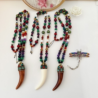 Três colares coloridos com pendentes em forma de cornos e um broche de libélula colorida