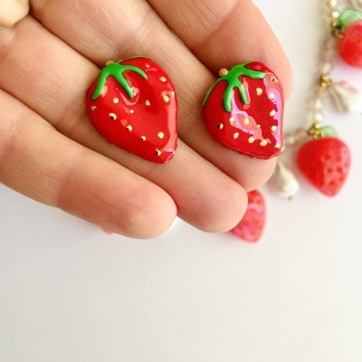 Brincos de morango vermelhos brilhantes com folhas verdes na mão