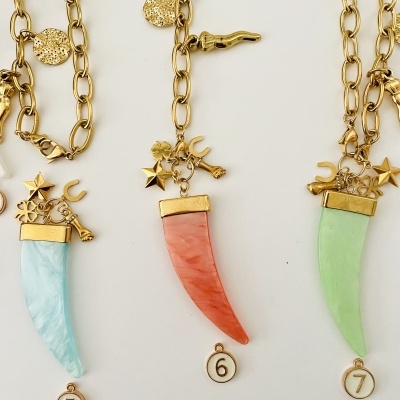 Três colares dourados com pingentes em forma de dente colorido e etiquetas numeradas