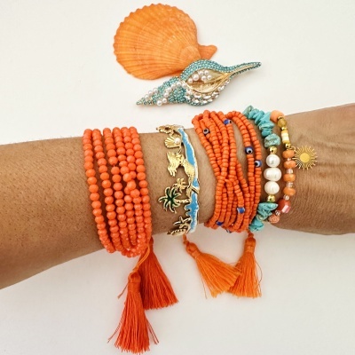 Pulseiras coloridas e broche em forma de concha sobre braço e fundo branco