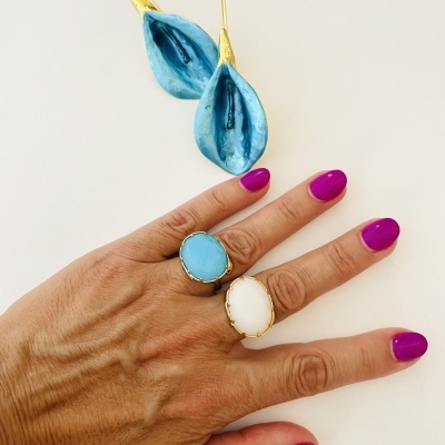 Anéis com pedras azul e branca em mão com unhas roxas, pendente azul e dourado