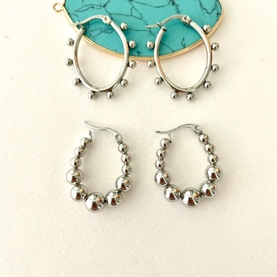 Dois pares de brincos de argola prateados com esferas, sobre superfície clara e suporte decorativo azul