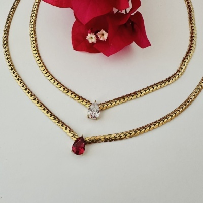 Colares dourados com pedra branca e vermelha sobre fundo branco e flor vermelha