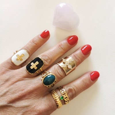 Mão com anéis dourados variados e unhas vermelhas sobre fundo branco com cristal em forma de coração.