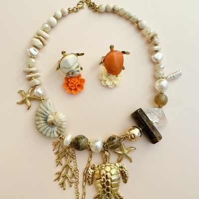 Conjunto de colar com pingentes marinhos dourados e brincos com flores laranja e branco