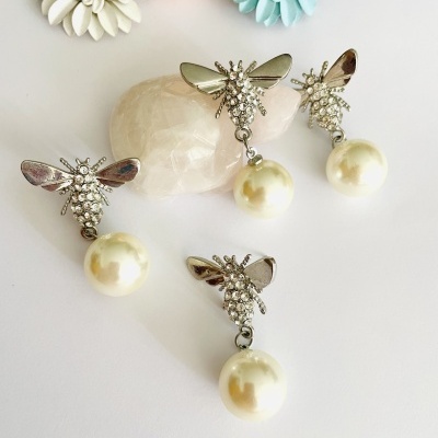 Brincos prateados de abelha com pérolas sobre fundo branco com flores artificiais