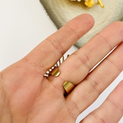 Mão a segurar acessório dourado, fundo com objeto oval e flor branca.