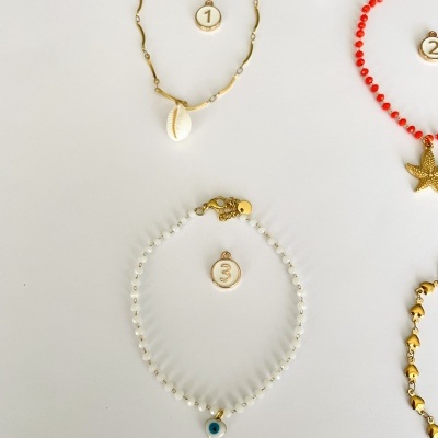Três pulseiras numeradas com diferentes pedras e pendentes em fundo claro.