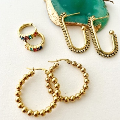 Três pares de brincos dourados com pedra decorativa verde azulada ao fundo