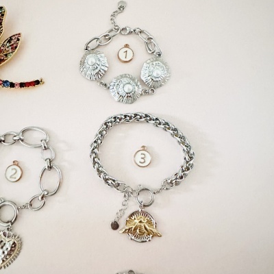 Três pulseiras metálicas prateadas numeradas com etiquetas de madeira em fundo claro