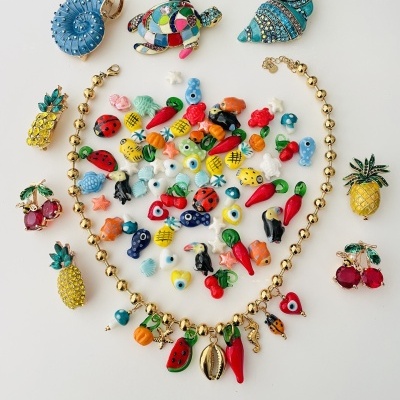 Colar dourado com pendentes coloridos de frutas e animais junto a miniaturas coloridas em fundo branco