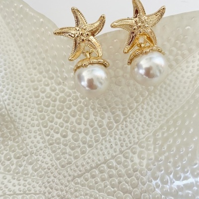 Brincos com estrela-do-mar dourada e pérola branca sobre superfície texturada