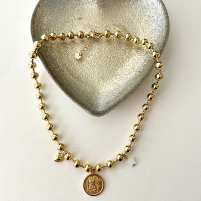 Colar dourado com pendente redondo numa bandeja em forma de coração cinzento