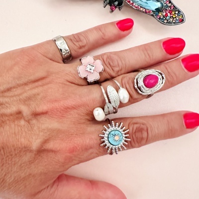 Mão feminina com cinco anéis diferentes em prata e unhas vermelhas