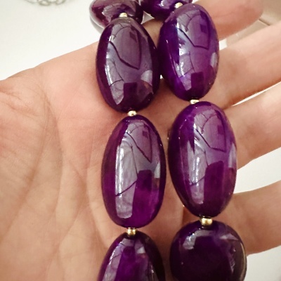 Colar de pedras ovais roxas brilhantes com contas douradas na mão.