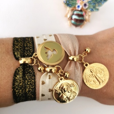 Três pulseiras elásticas com medalhões dourados e um broche de abelha colorido ao fundo