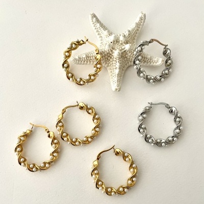 Brincos de argola dourados e prateados com pérolas, dispostos sobre uma superfície branca com estrela-do-mar decorativa.