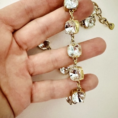 Pulseira dourada com pedras transparentes facetadas segurada por mão