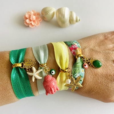 Pulseiras coloridas com pendentes dourados num pulso e conchas ao fundo