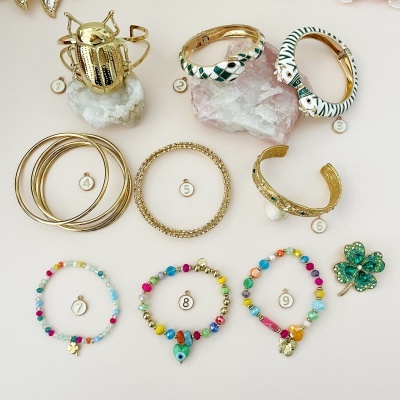 Coleção de pulseiras, anel dourado em forma de escaravelho e broche verde em forma de trevo sobre fundo branco