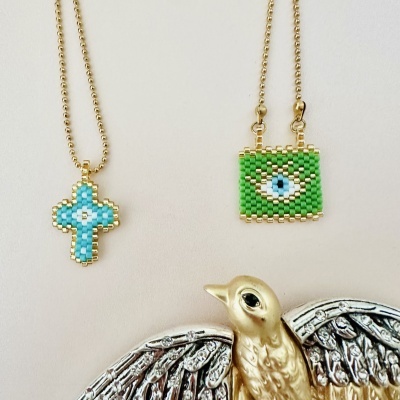 Colares com pendentes de contas em forma de cruz azul e retângulo verde com olho, correntes douradas, figura dourada com asas prateadas.