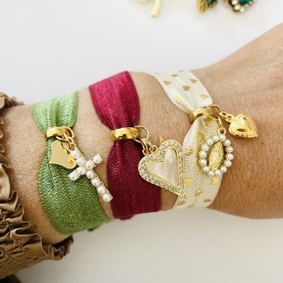 Pulseiras coloridas com pingentes dourados e pérolas num pulso sobre fundo branco