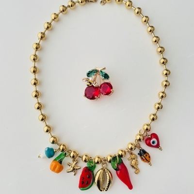Colar dourado com pendentes coloridos e alfinete de cereja com pedras vermelhas sobre fundo branco