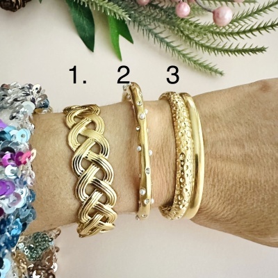 Braceletes dourados numerados 1, 2 e 3 no pulso com folhas verdes ao fundo