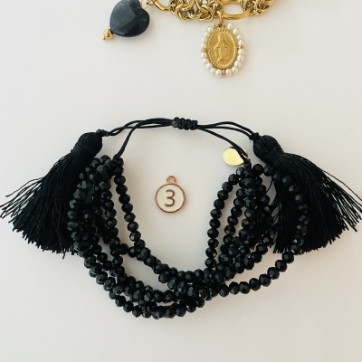 Duas pulseiras, uma dourada com pendentes e outra preta com contas e franjas.