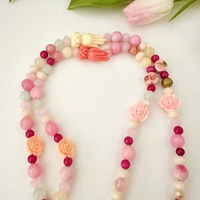 Colar colorido com contas redondas e florais e pingentes em forma de mão, junto a uma tulipa rosa.