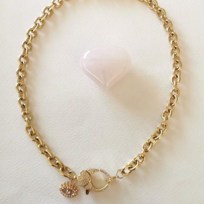 Colar dourado com pendente em forma de olho e um objeto rosa em forma de coração