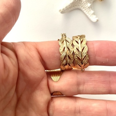 Duas pulseiras douradas com padrão de folhas sobre dedos de uma mão, estrela-do-mar ao fundo