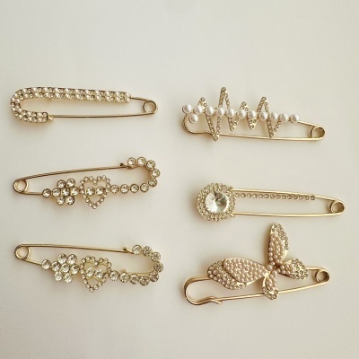 Seis alfinetes dourados decorativos com pedras e pérolas em fundo claro